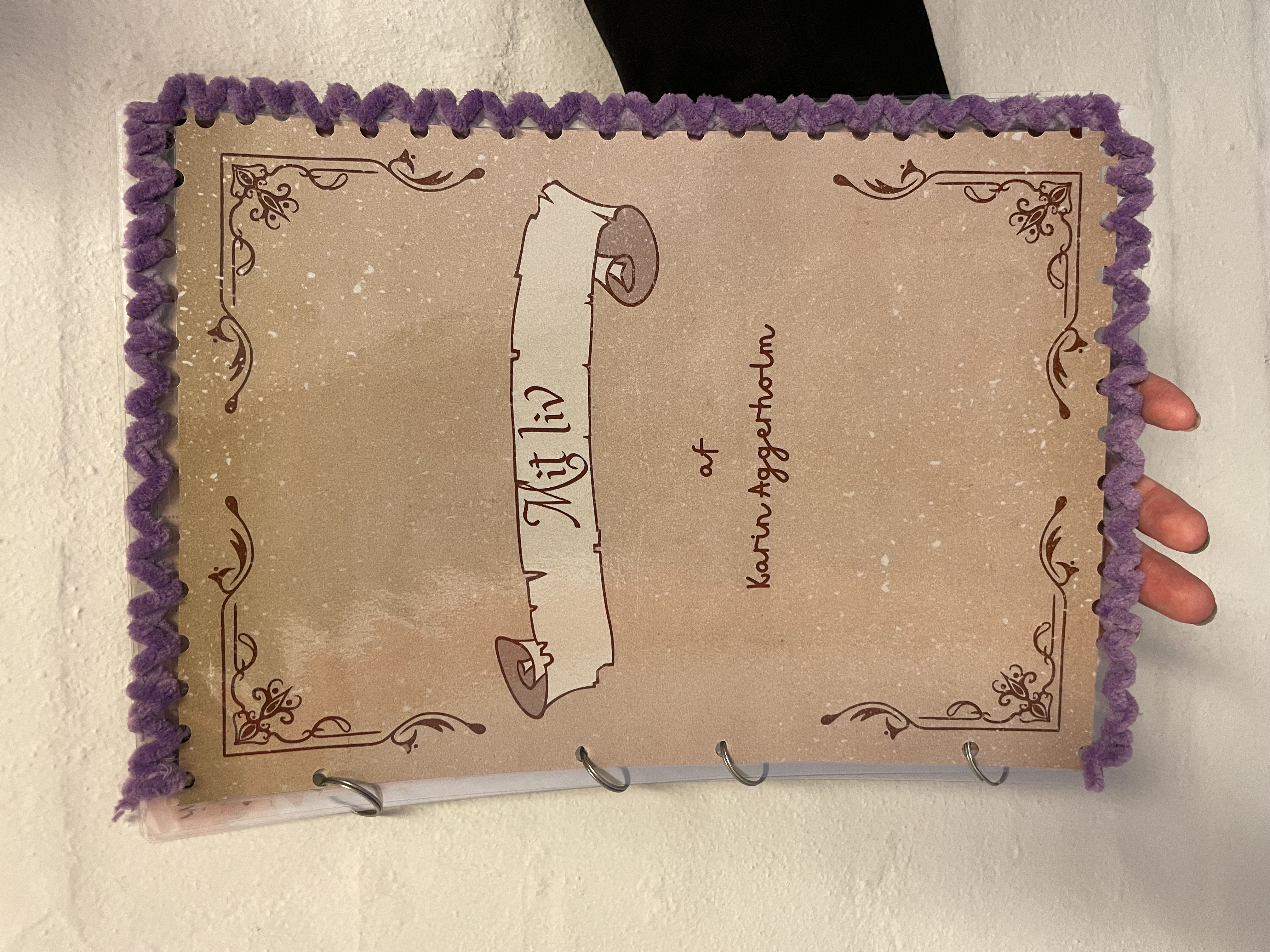Karins flotte bog "Mit liv". Bogen er lavet af lamineret papir i en brun nuance. Rundt i kanten er trukket lilla garn, som er Karins eget. 