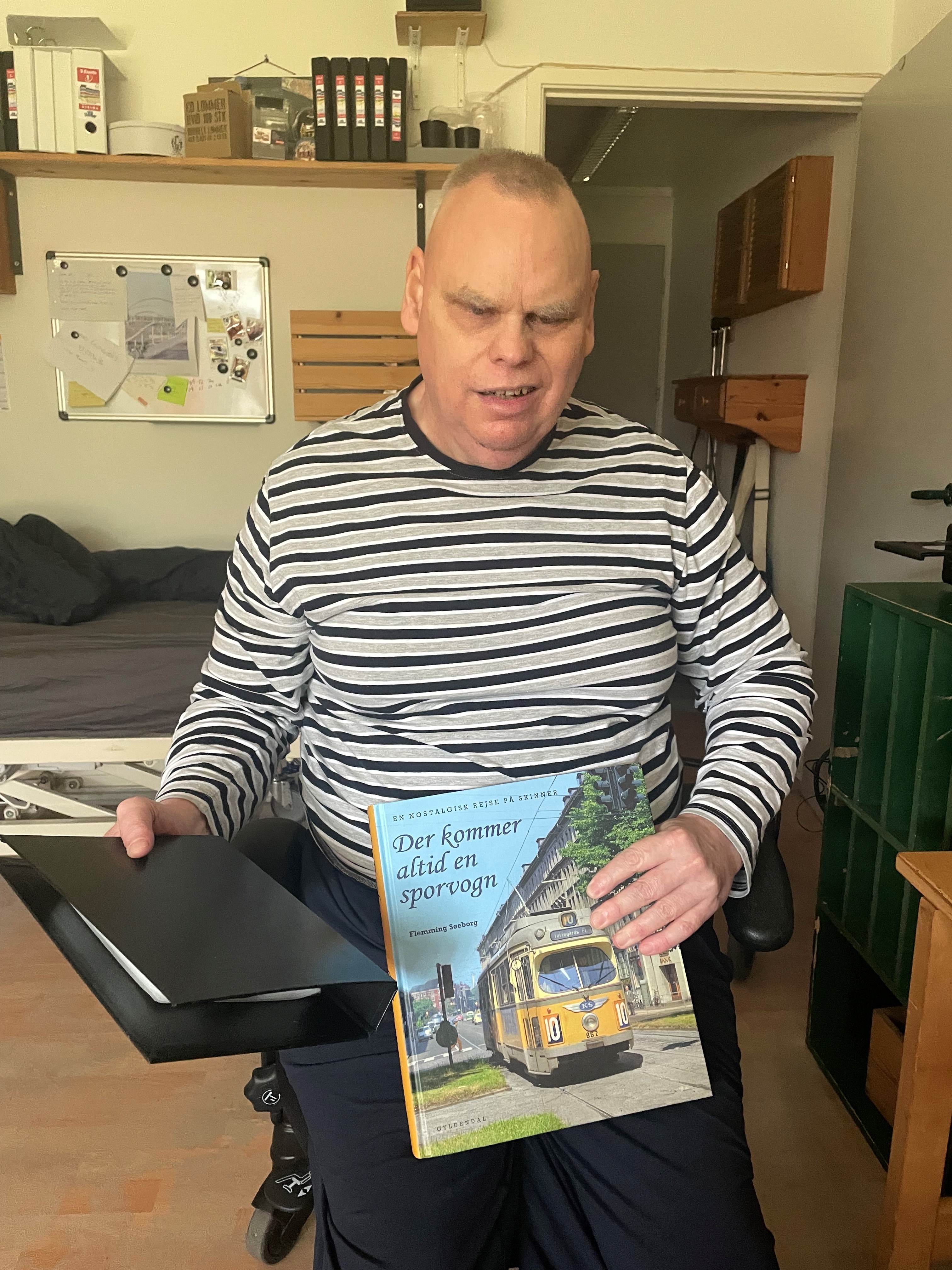 Dan i sin lejlighed med en bog om sporvogne i den ene hånd og hans mappe med lydbøger i den anden. 