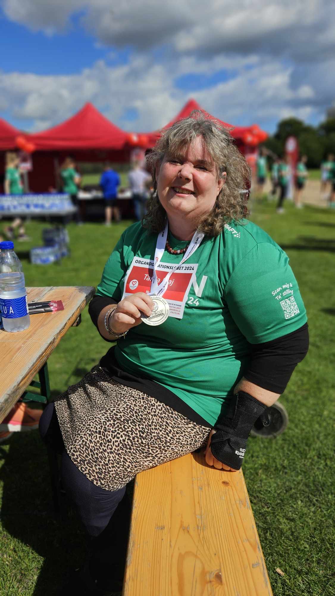 Glade og stolte Tanja sidder på en bænk og får sig en forfriskning. Tanja har sin flotte medalje om halsen.