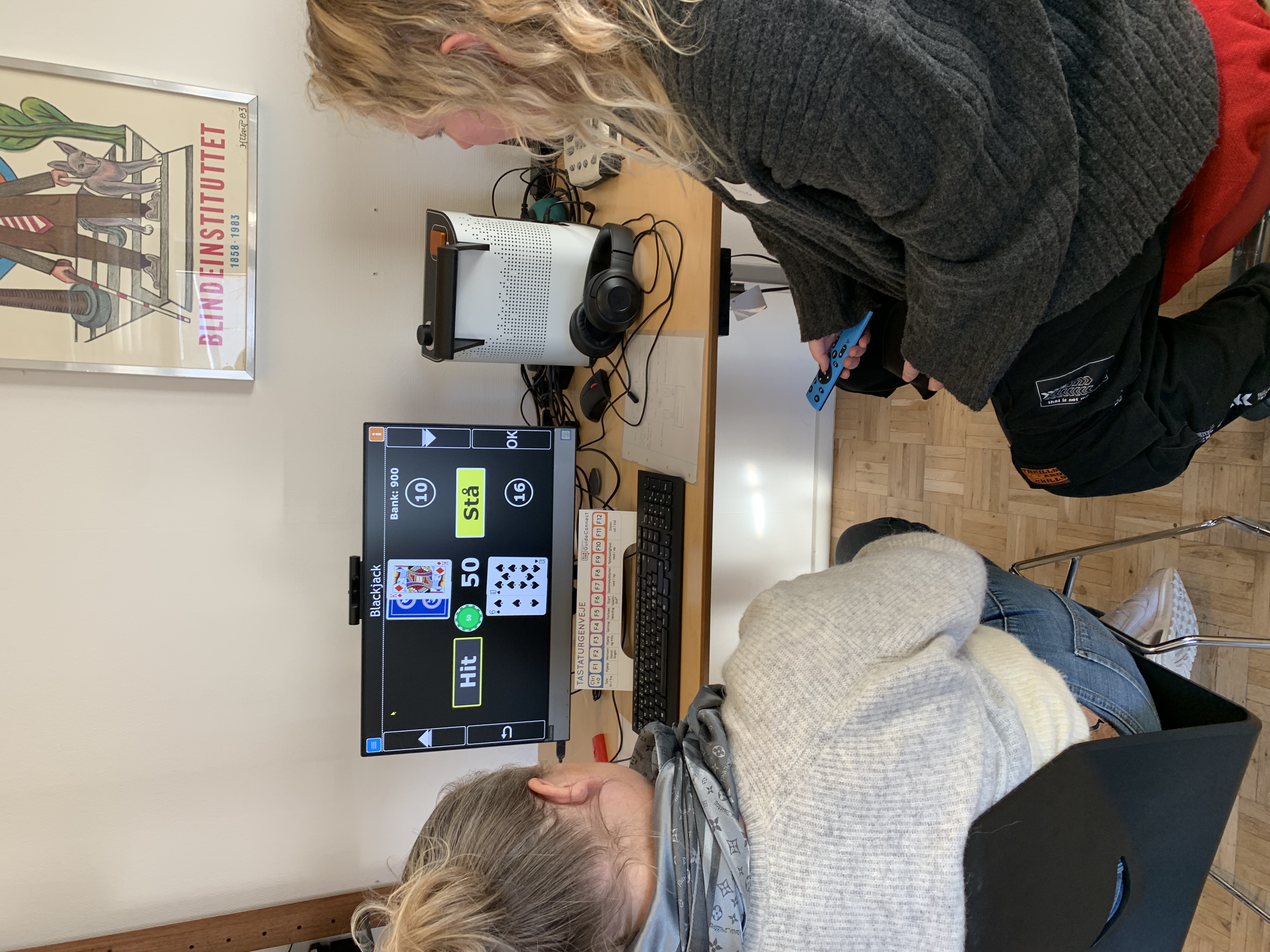 Under modulet om synet og synsfaglighed er der en masse praktiske opgaver. Her er det Nita og Helena, der spiller en omgang blackjack og afprøver Guide Connect, som er et kompenserende program til PC med skærmlæserfunktion. Helena sidder med programmets fjernbetjening, som kan bruges i stedet for tastaturet. Man kan også tale ind i fjernbetjeningen, hvorefter den omdanner tale til tekst. Det er vigtigt, at medarbejderne får indsigt i de forskellige synskompenserende muligheder, så de bedst muligt kan støtte beboerne og brugerne. 